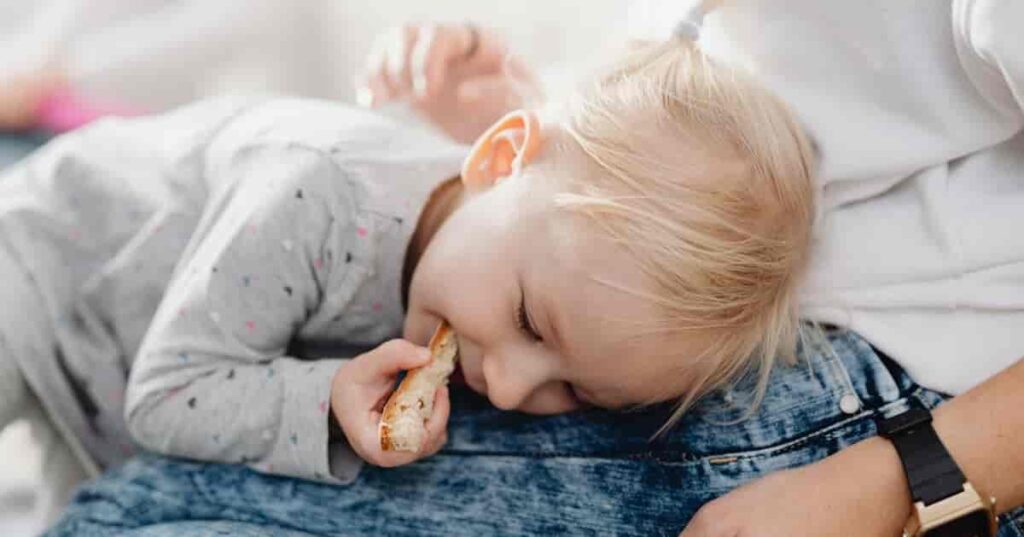 A Girl Eating Bread while Lying Down on Her Mother's Lap
